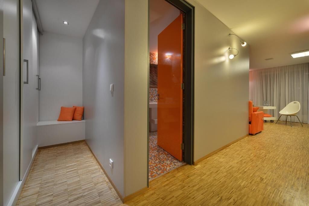 Habitació d'hotel moderna amb terra de fusta, zona de seients amb coixins taronja, una cadira blanca i una taula petita.