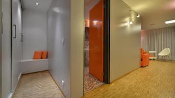 Habitació d'hotel moderna amb terra de fusta, zona de seients amb coixins taronja, una cadira blanca i una taula petita.