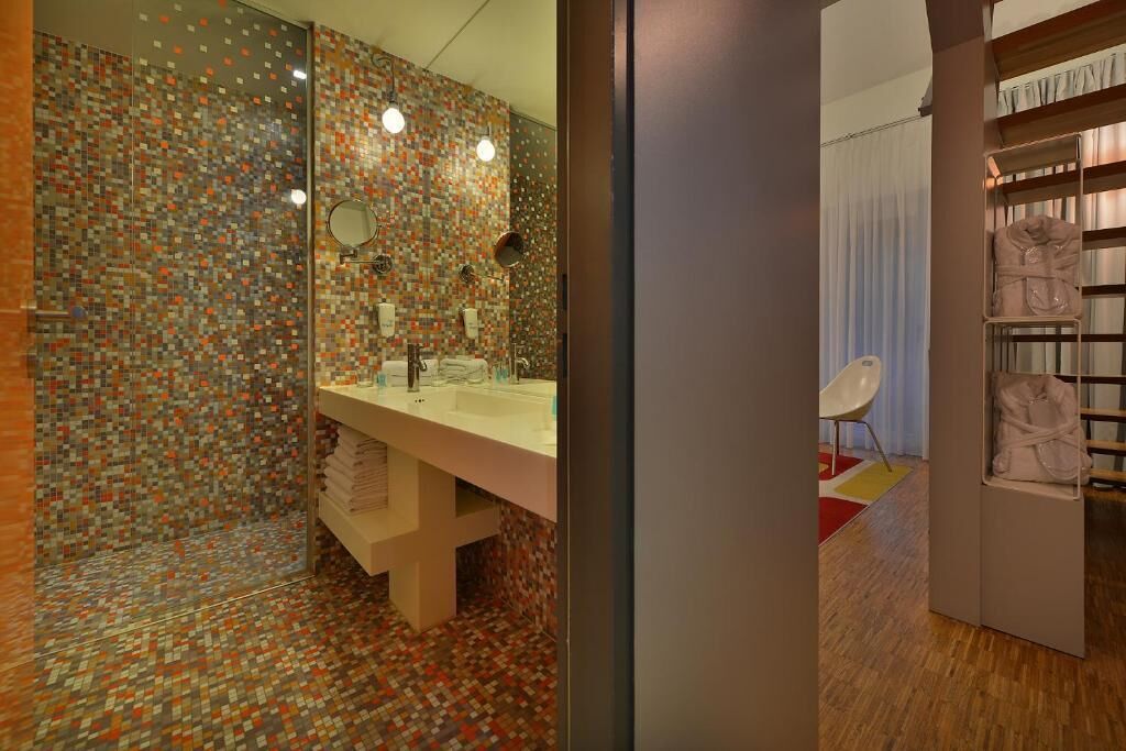 Une salle de bain moderne avec un mur recouvert de mosaïques, un grand miroir et un meuble-lavabo.