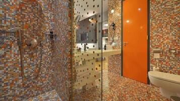 A modern bathroom with mosaic tile walls, a glass shower enclosure, a white toilet, and an orange door.