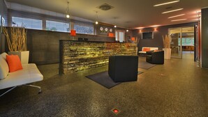 A modern lobby with a reception desk, seating area, and a stone wall feature. - Omnia Hotel Relax & Wellness (Janske Lazne)