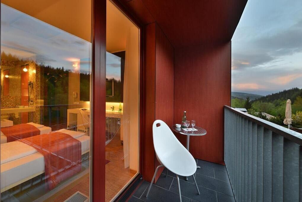 Un balcón con puerta de vidrio que da a un área de spa, una silla blanca y una mesita con una botella y vasos.