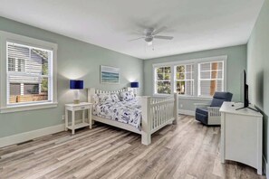 A bedroom with a bed, bedside tables, a desk, a chair, a ceiling fan, and windows with blinds.