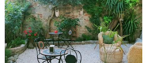 An outdoor seating area with a table and chairs, surrounded by plants and a stone wall.