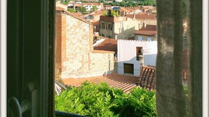 A view through a window of a town with buildings, greenery, and distant hills. - La Belle D'Âme (Prades)
