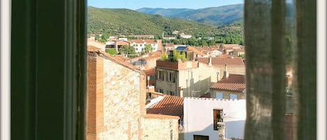 A view through a window of a town with buildings, greenery, and distant hills.