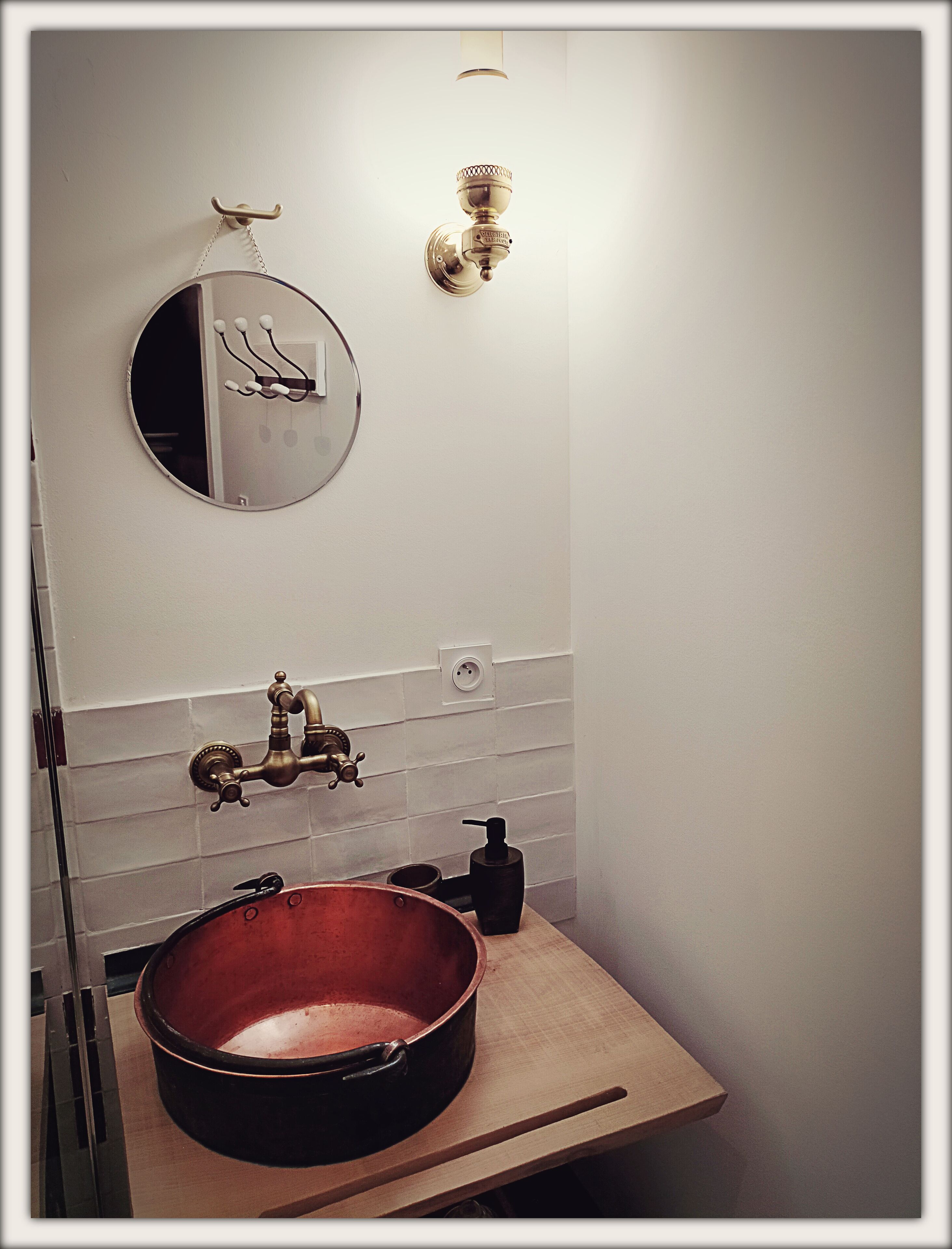 A bathroom with a round mirror, a copper sink, a faucet, and a wall-mounted light fixture.