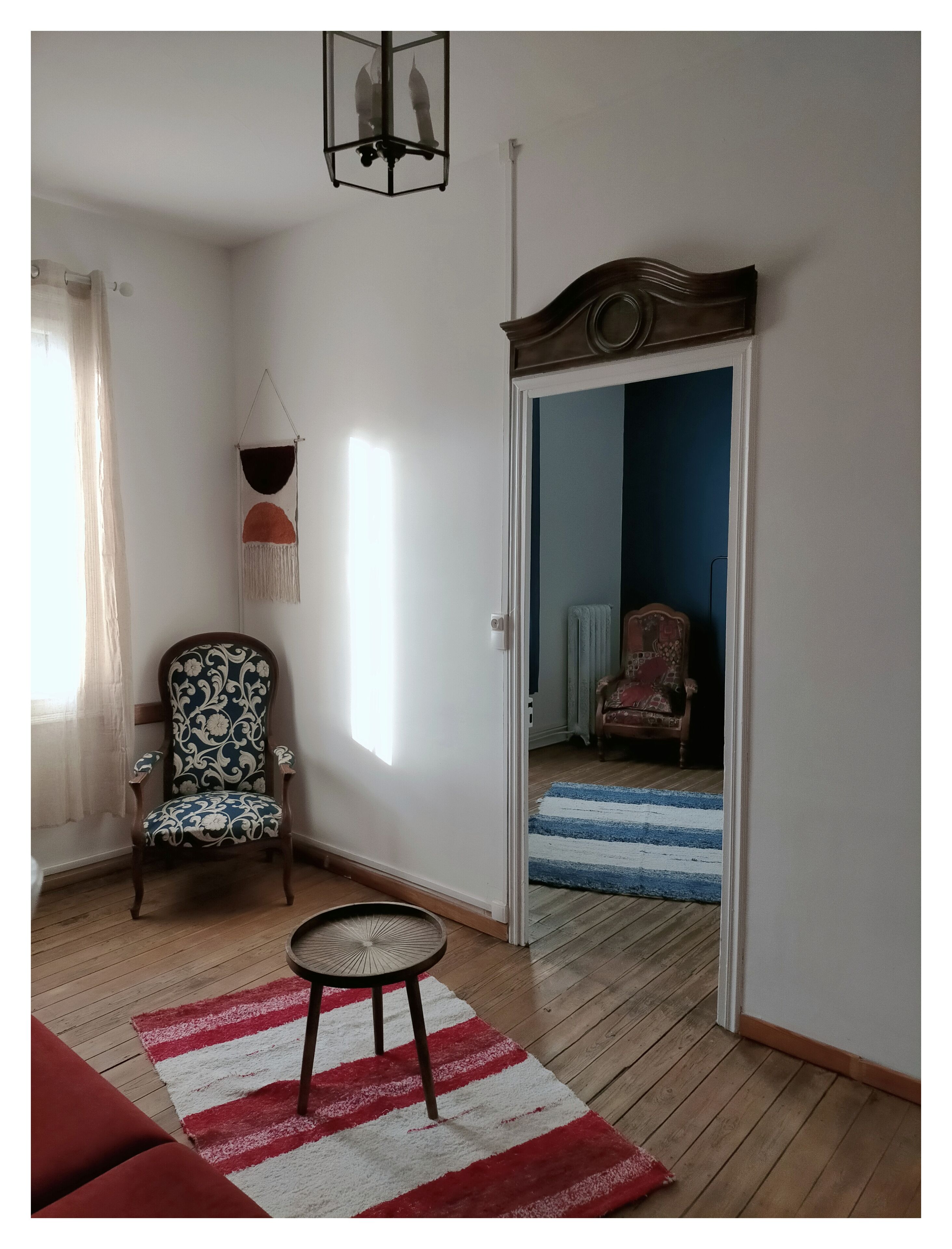 A living room with a patterned armchair, a small round table, a red and white striped rug, and a wooden floor.
