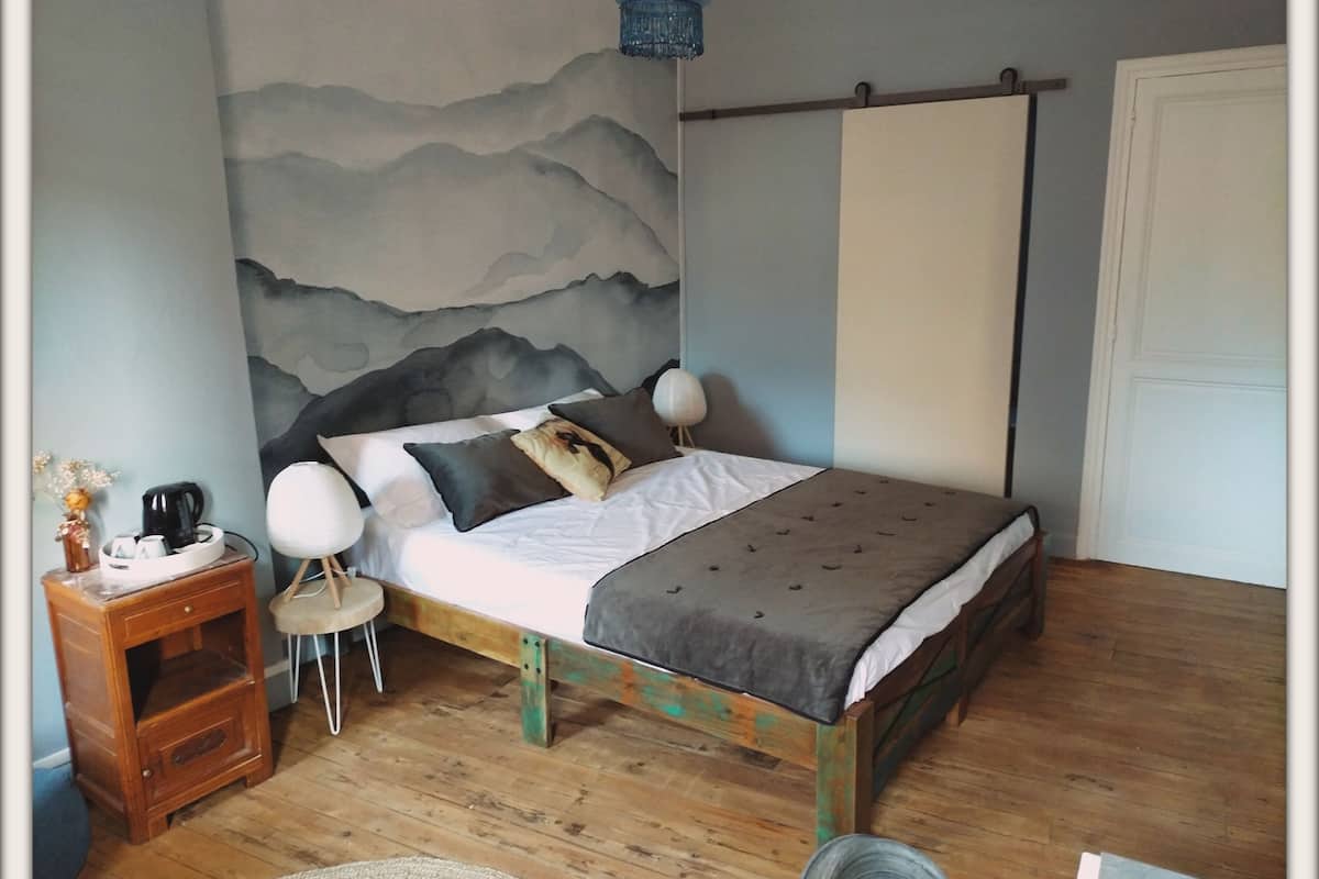Un dormitorio con cama, mesita de noche, lámpara y un mural en la pared.