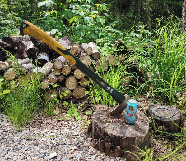 A log pile, a hammer, and a can on a tree stump.