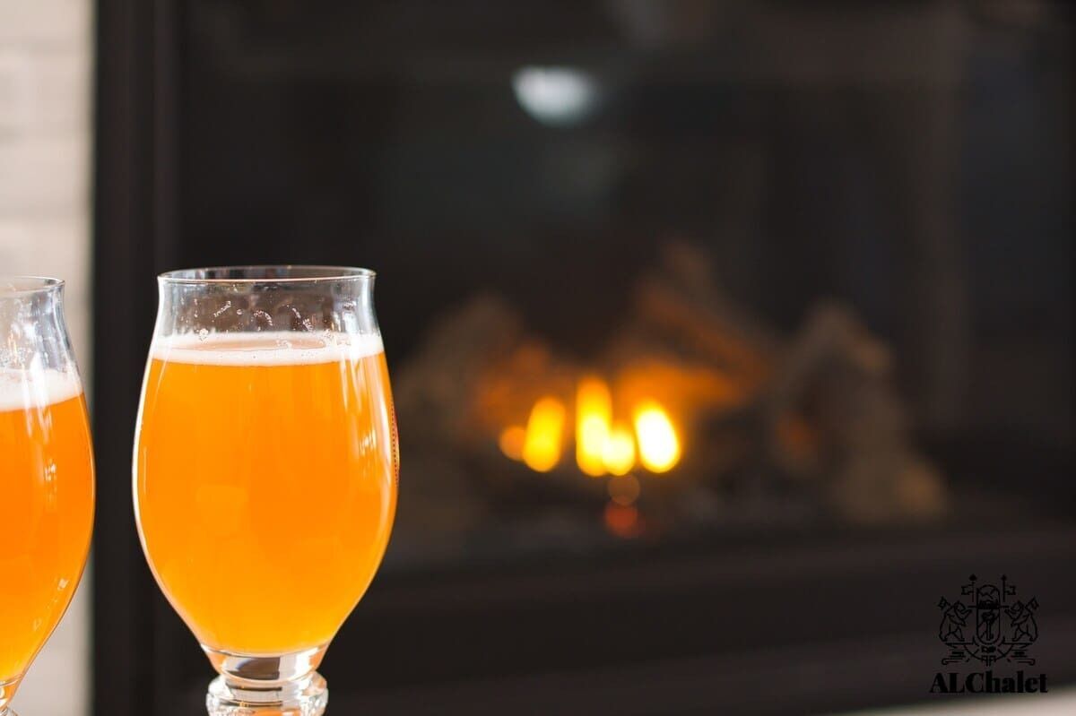 Two glasses of beer in front of a fireplace.