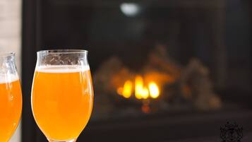 Two glasses of beer in front of a fireplace.