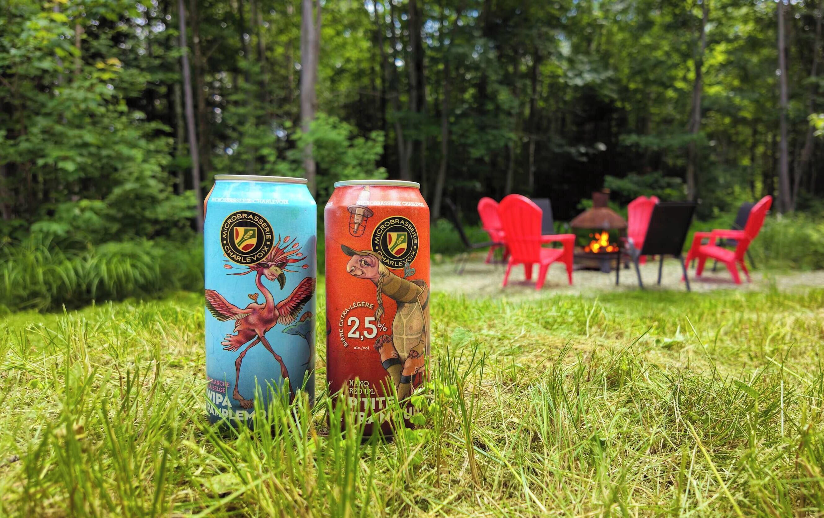 Two beverage cans on grass with a forest and outdoor seating in the background.