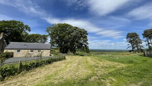 A stone house with a sloped roof, surrounded by a grassy field and trees. - Romantic 1 bedroom Rural Retreat with spectacular views across Northumberland (Hexham)