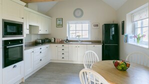 A kitchen with white cabinets, a wooden ceiling, a clock, a sink, a refrigerator, and a dining table with chairs. - Romantic 1 bedroom Rural Retreat with spectacular views across Northumberland (Hexham)