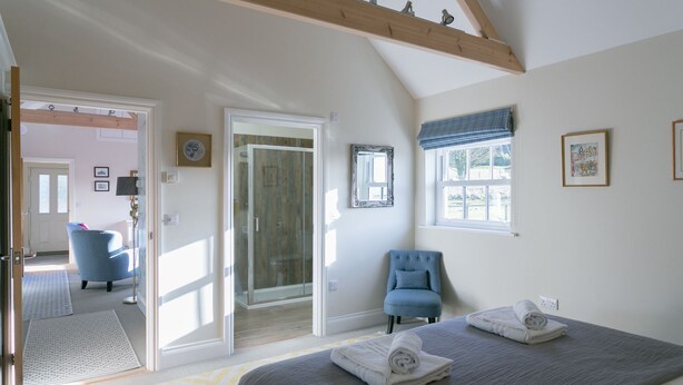 A bedroom with a large bed, a chair, a door leading to another room, and a window with a view. - Romantic 1 bedroom Rural Retreat with spectacular views across Northumberland (Hexham)