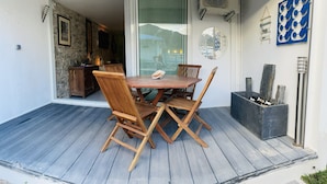 Ett träbord med fyra stolar på ett trädäck, ett litet skåp och en väggmonterad luftkonditioneringsanläggning.