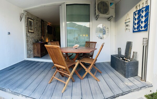 A wooden table with four chairs on a wooden deck, a small cabinet, and a wall-mounted air conditioner.