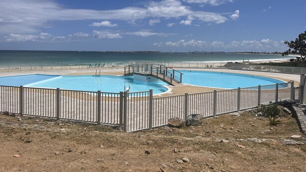 Ett poolområde med två pooler, en strand och en klar himmel.