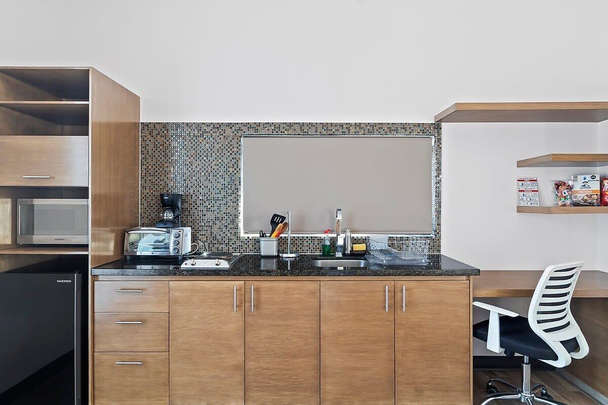 A compact kitchen with a microwave, toaster, and coffee maker on the countertop, a sink, and a chair.