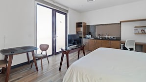 Una moderna camera d'albergo con un letto grande, un tavolo da pranzo con sedie, angolo cottura e una porta scorrevole in vetro che dà sull'esterno.
