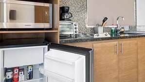 Una cucina moderna con forno a microonde, tostapane e macchina per il caffè integrati. Il frigorifero è aperto, mostrando bevande e lattine.
