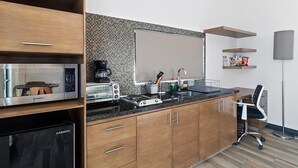Una cucina moderna dotata di forno a microonde, tostapane e macchina del caffè. Si nota un lavello con rubinetto e un armadietto con cassetti. Una sedia è posizionata vicino al lavello, e si intravede una piccola mensola con oggetti.