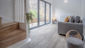 Ein modernes Wohnzimmer mit einem grauen Sofa, einem Korbstuhl und einer Treppe mit Holzdielen.