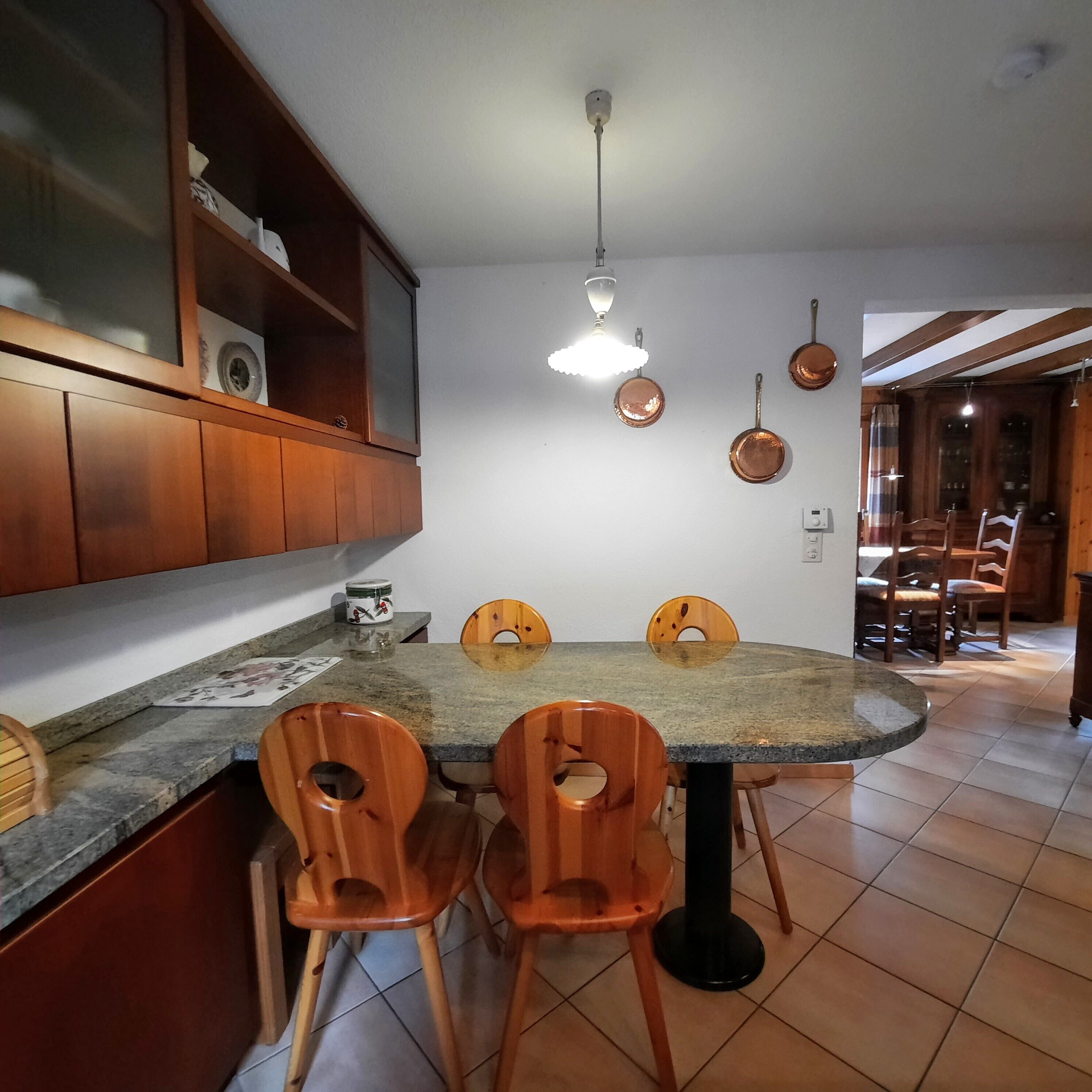 A kitchen with a dining table, wooden chairs, a hanging light fixture, and a cabinet with a glass door.