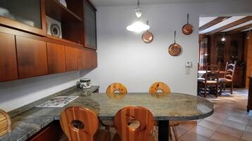 A kitchen with a dining table, wooden chairs, a hanging light fixture, and a cabinet with a glass door.
