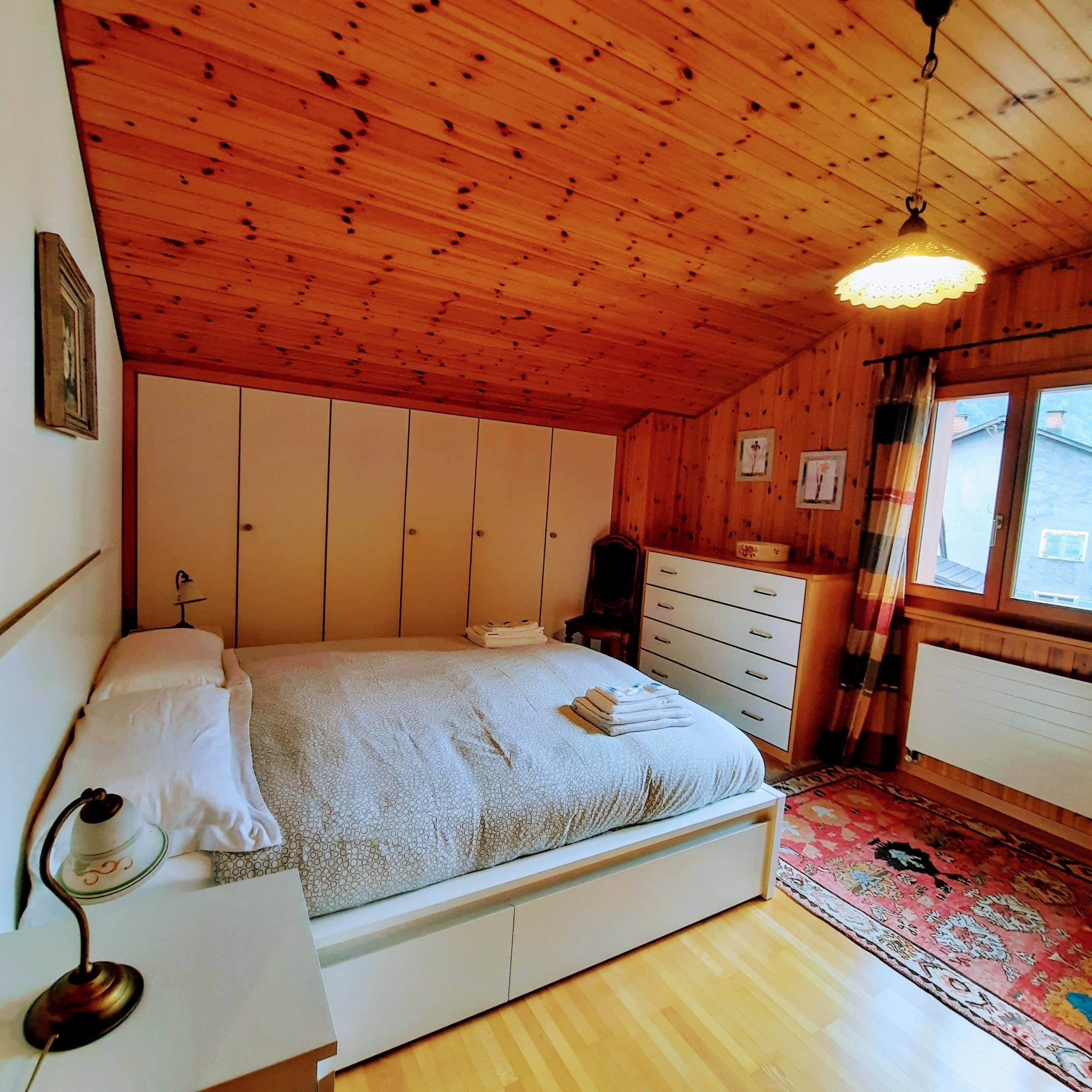 A wooden-paneled bedroom with a bed, dresser, and a window with curtains.