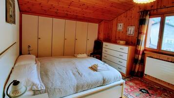 A wooden-paneled bedroom with a bed, dresser, and a window with curtains.