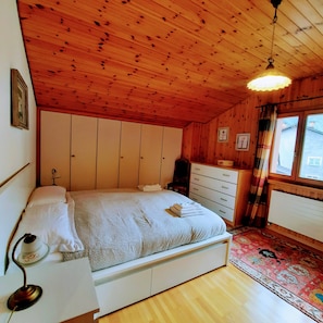 A wooden-paneled bedroom with a bed, dresser, and a window with curtains. - Chalet Nucleo 12 (Faido)