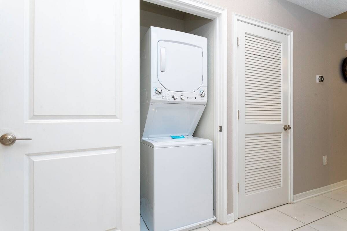 A laundry room with a stacked washer and dryer, white doors, and a tiled floor.