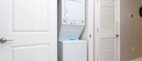 A laundry room with a stacked washer and dryer, white doors, and a tiled floor.