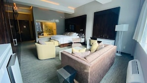 A modern hotel room with a large bed, a sofa, a coffee table, and a TV. There is a large window and a door leading to another room. - Room in luxurious downtown property (St. John's)