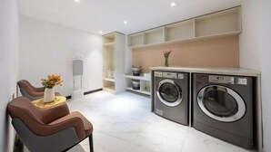 A modern laundry room with two front-loading washing machines, a small seating area with a table and chairs, and built-in shelving above the machines. - Starway Hotel (Beijing Yanqi Development Zone) (Beijing)