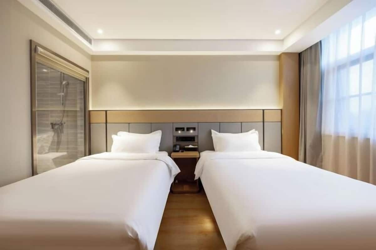 A hotel room with two beds, a bedside table, a nightstand, a mirror, and a window with curtains.