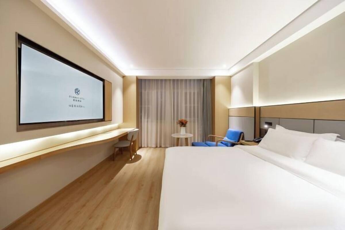 A hotel room with a bed, a desk, a chair, a TV, and a window with curtains.
