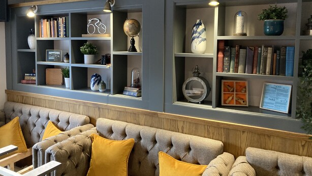 A room with a grey wall, a bookshelf, and a tufted sofa with yellow cushions. - Old Swan (Skipton)