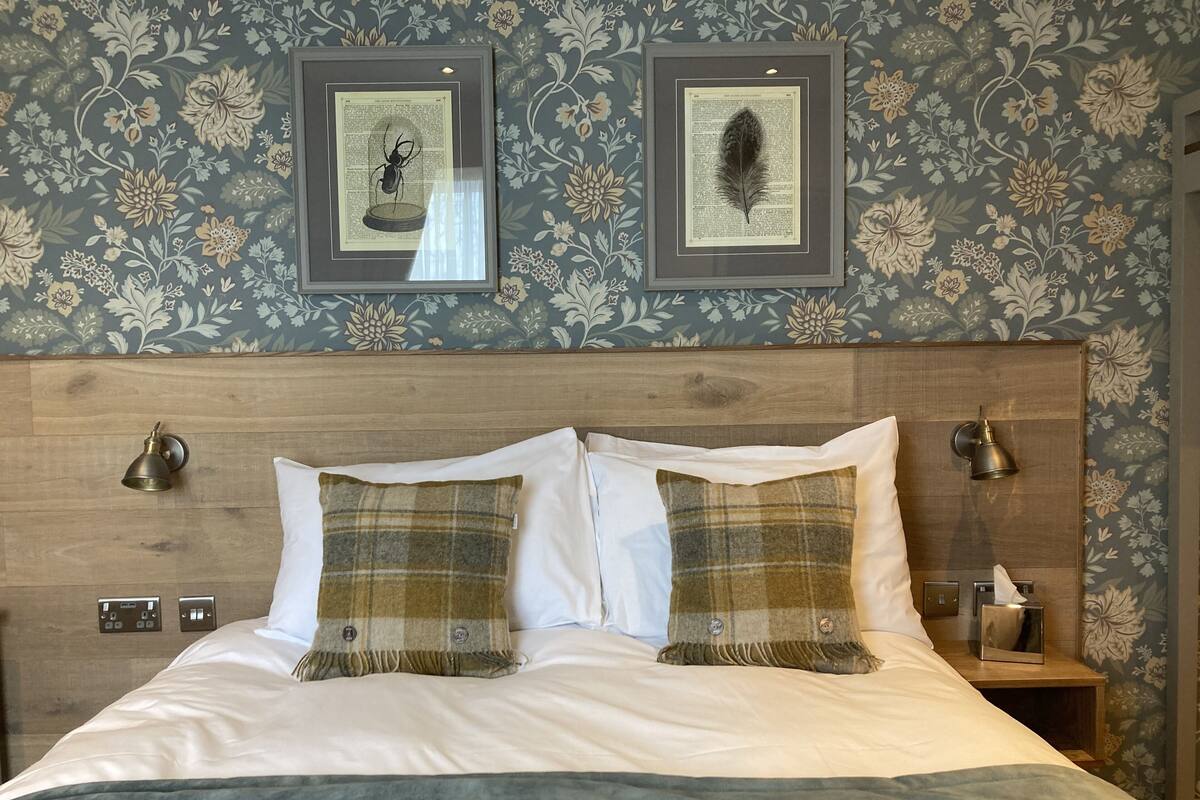 A neatly made bed with two pillows, a wooden headboard, and framed wall art above.