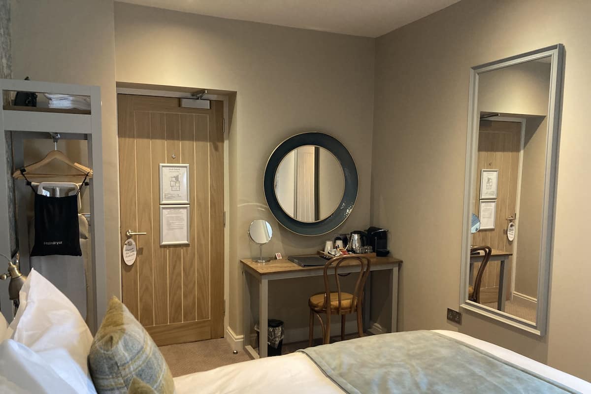 A hotel room with a bed, a desk with a chair, a large mirror, and a wardrobe.