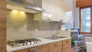 A modern kitchen with a gas stove, stainless steel range hood, and a built-in oven. There is a sink with a faucet and a window providing natural light. - Alle mura apartment (Verona)