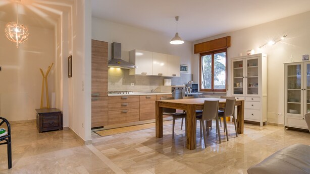 A modern kitchen with a dining area, wooden cabinets, and a large window. - Alle mura apartment (Verona)