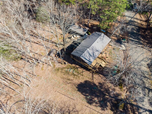 Luchtbeeld van een huis met een metalen dak, omgeven door bomen en een onverharde voortuin.