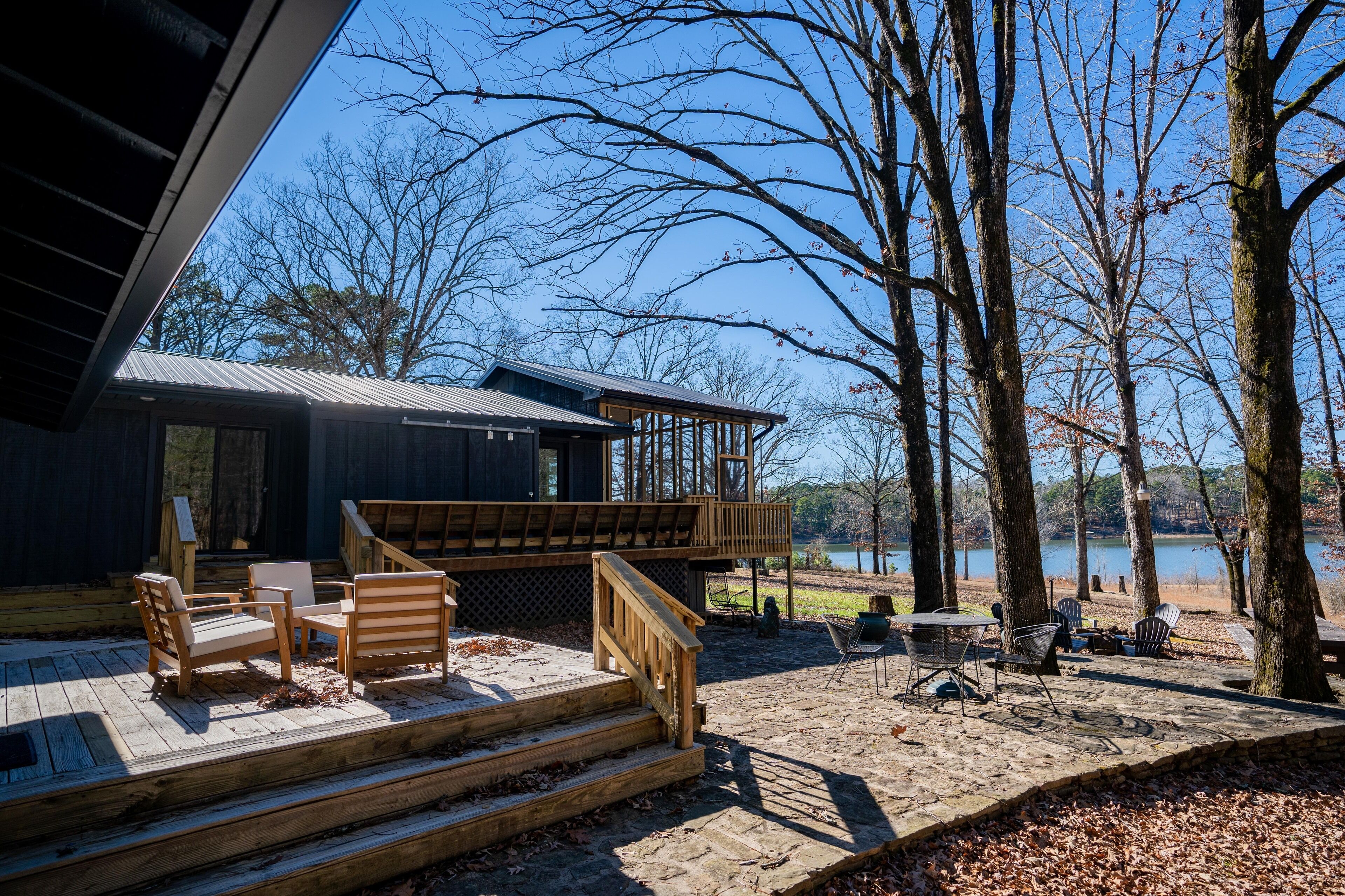 A wooden deck with outdoor seating, a staircase leading to a covered area, and a view of a lake.