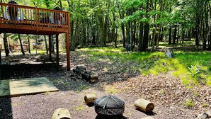 A forested area with a wooden deck, a fire pit, and logs. - IML -NearJim Thorpe-Pets Allowed🐕‍🦺 Free, Sleeps10 (Albrigthsville)