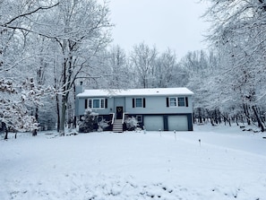 Uma casa de dois andares com garagem, rodeada por árvores cobertas de neve.
