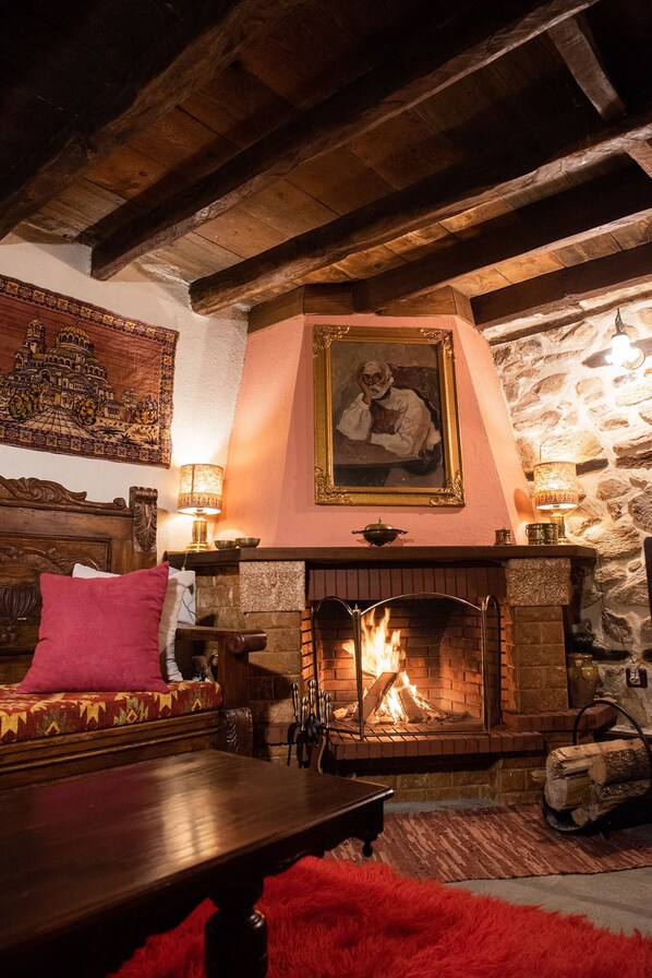 A cozy room with a fireplace, wooden beams, a cushioned bench, and a red rug.