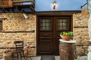 A stone building with a wooden door, a chair, a small table with a drink, and a potted plant.